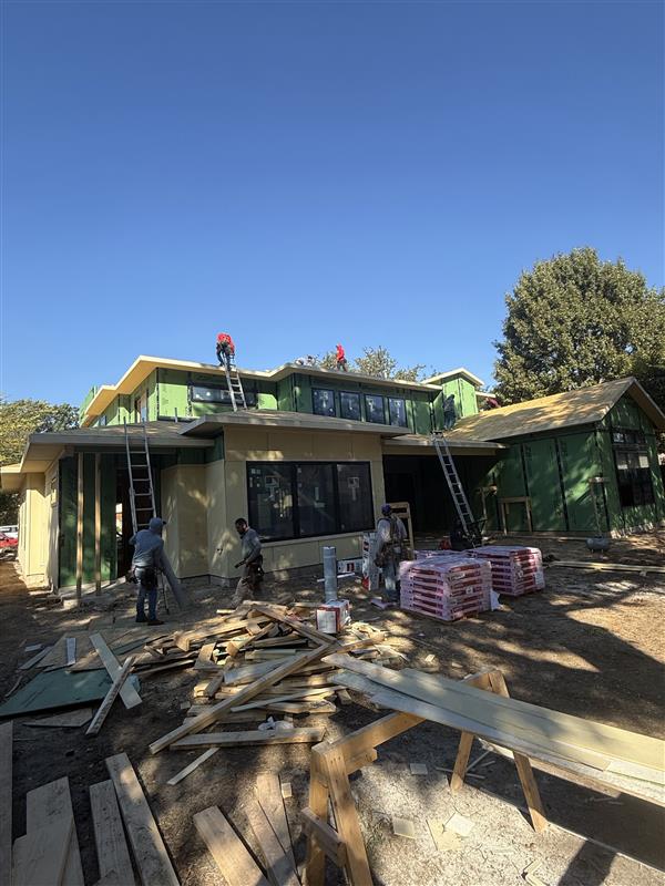 Phase 8 — Roof framing and decking underway with crew installing shingles