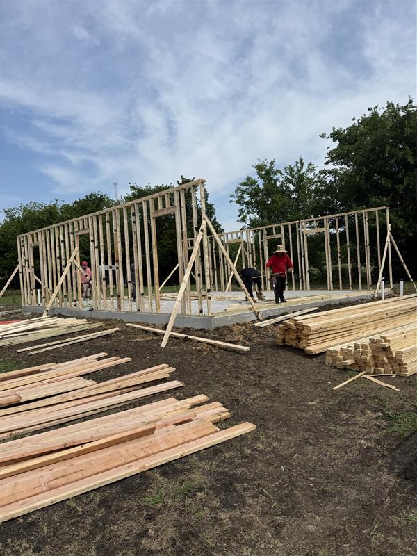 Phase 2 — Wall framing underway with lumber stacks staged on site